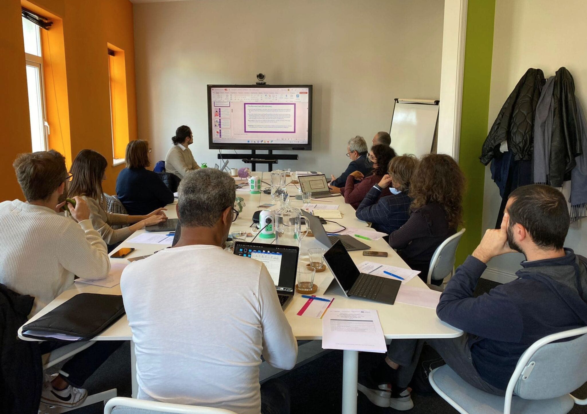 equipo de housing care reunido en una mesa mirando a una pantalla digital 