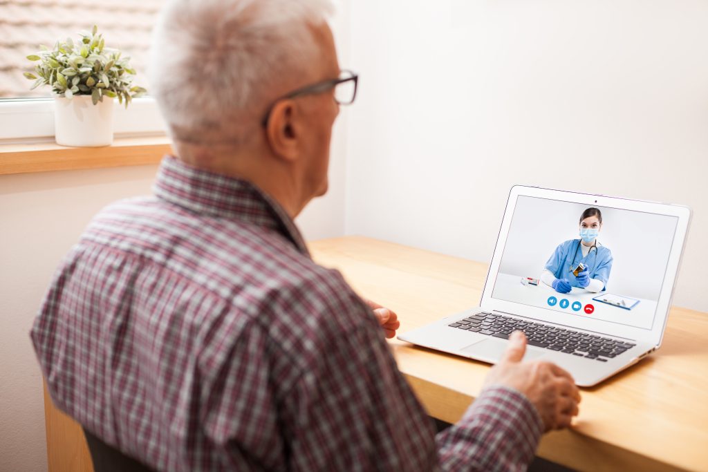 Young female UK e-doctor consulting elderly man, online video help line virtual medical appointment